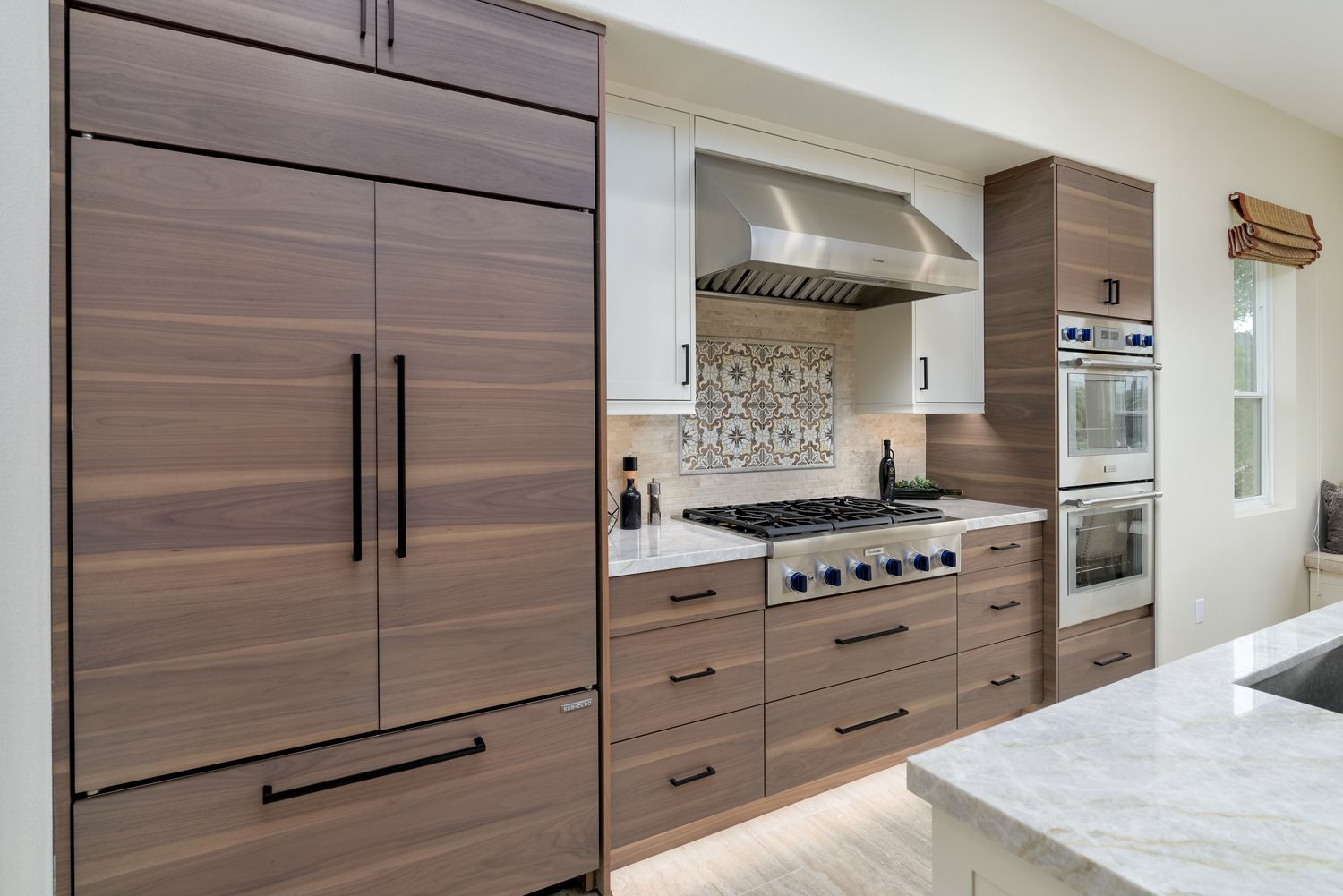 Modern kitchen with wood cabinets, stainless steel range hood, mosaic backsplash, and marble island countertop