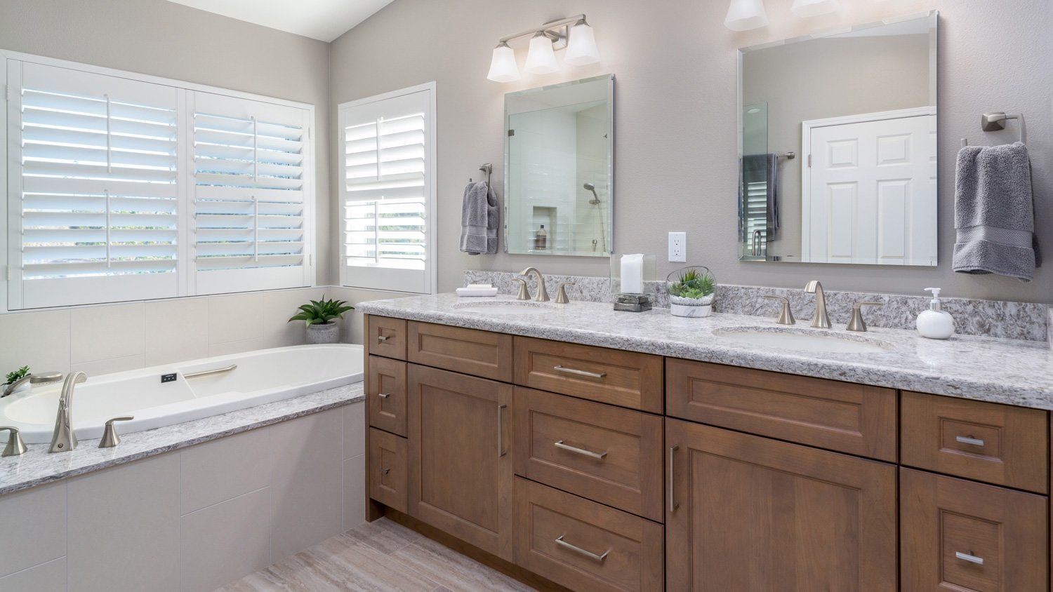 Bright bathroom with double vanity, large mirrors, soaking tub, and white shutters.