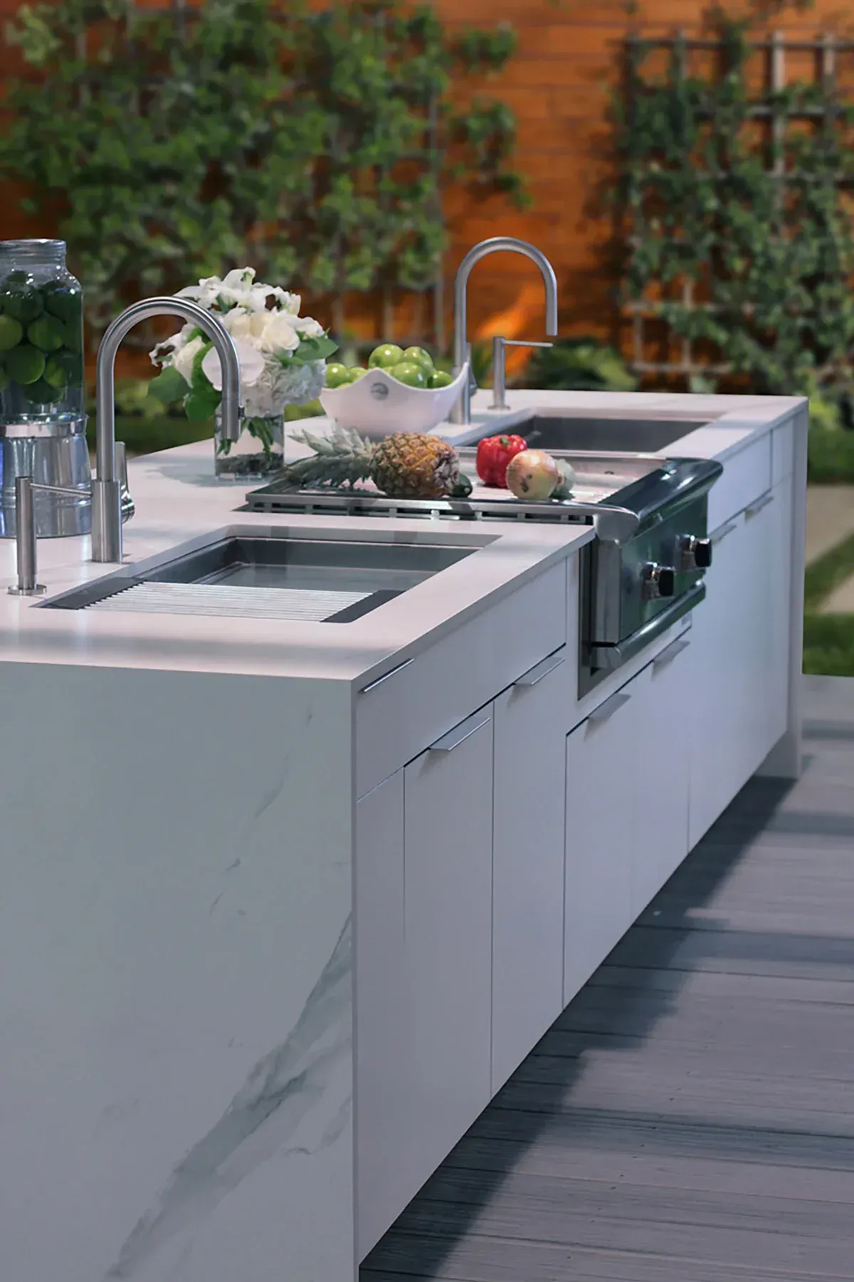 Modern outdoor kitchen island with sink, stovetop, and white marble finish on a patio