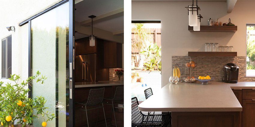 Modern kitchen interior with black cabinets, marble island, pendant lights, and a view of the patio through open glass doors
