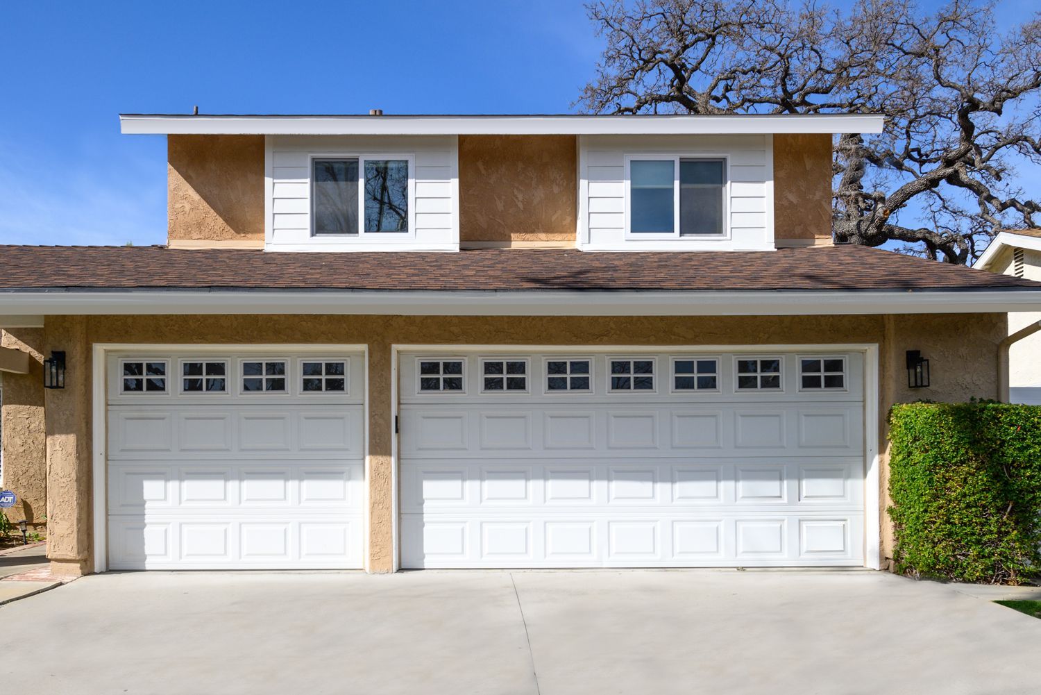 image shows the front exterior of a house with two white garage doors and two new white bay windows on the second floor. Oak Park, CA home remodel, widow replacement remodel 