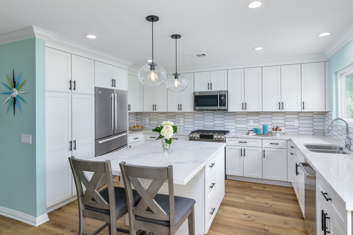 Bright white modern kitchen with island, stainless appliances, light blue walls, and two wooden stools