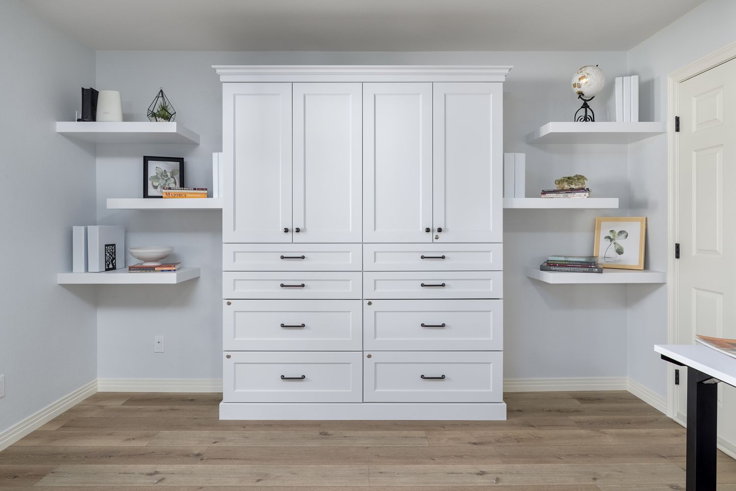 White built-in cabinets with shelves in a bright room, featuring books, decor, and a wooden floor.