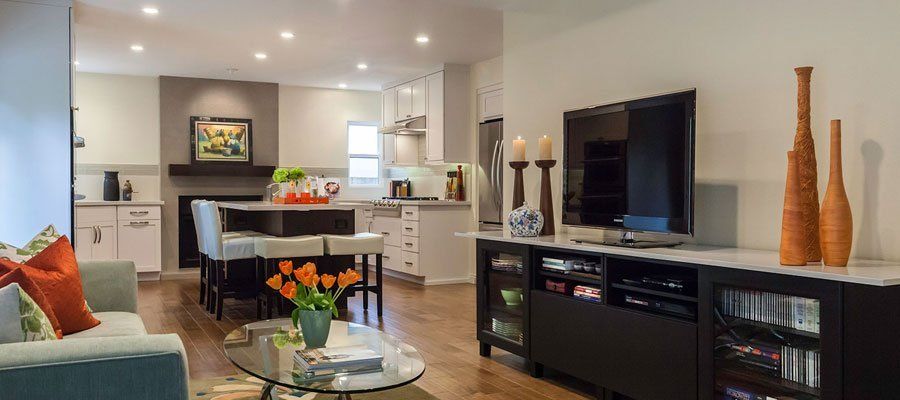 Bright open-concept living room with TV console, sofa, glass coffee table, and kitchen in the background