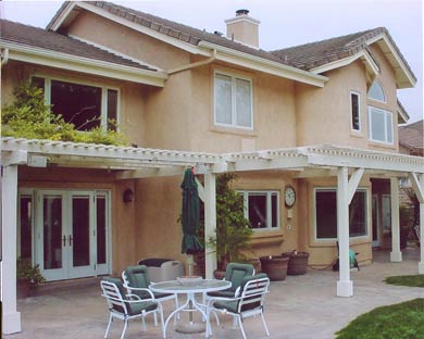 Two-story beige house with covered patio, white outdoor table and chairs, and potted plants