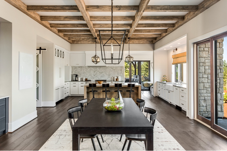 Bright modern kitchen and dining area with wooden beams, dark table, and large windows