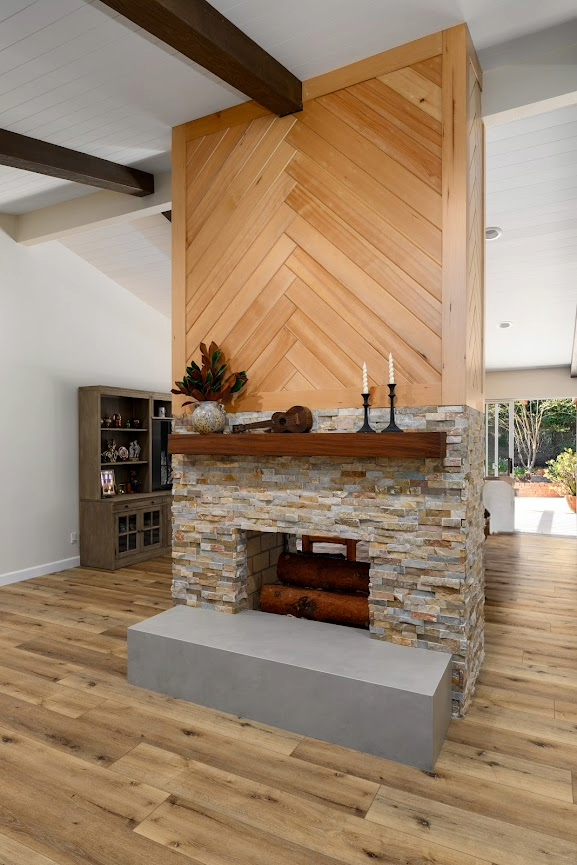 Stone fireplace with wood herringbone chimney in a bright living room with hardwood floors