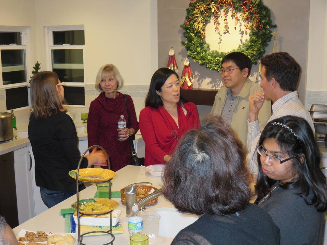 People chatting at a holiday party around a table with snacks and drinks, decorated fireplace in the background