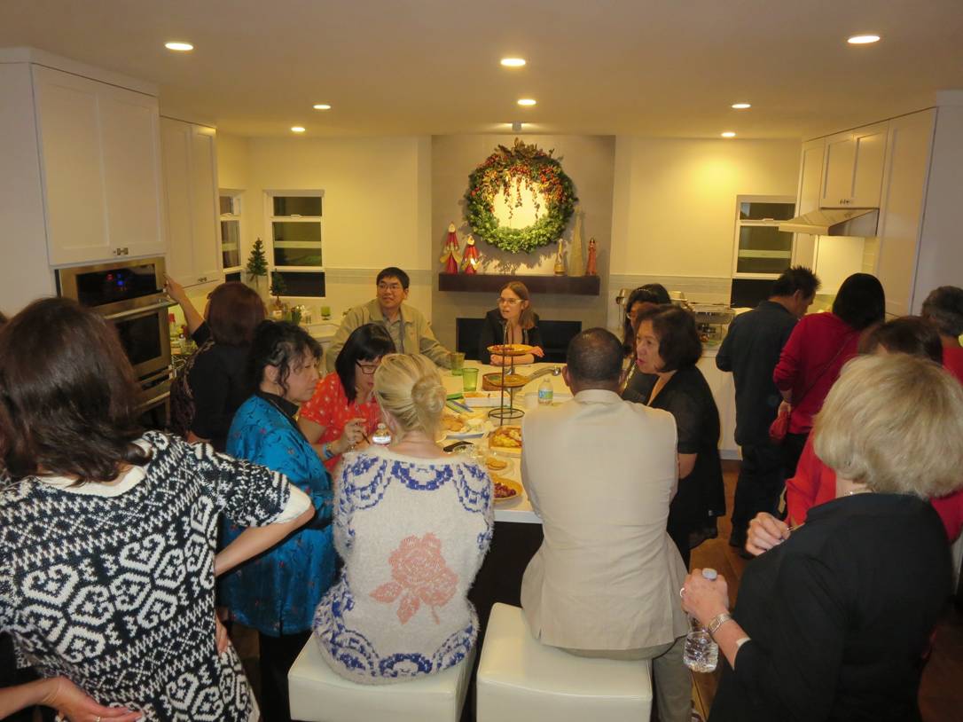 People seated around a table at a festive indoor gathering with a wreath on the wall.