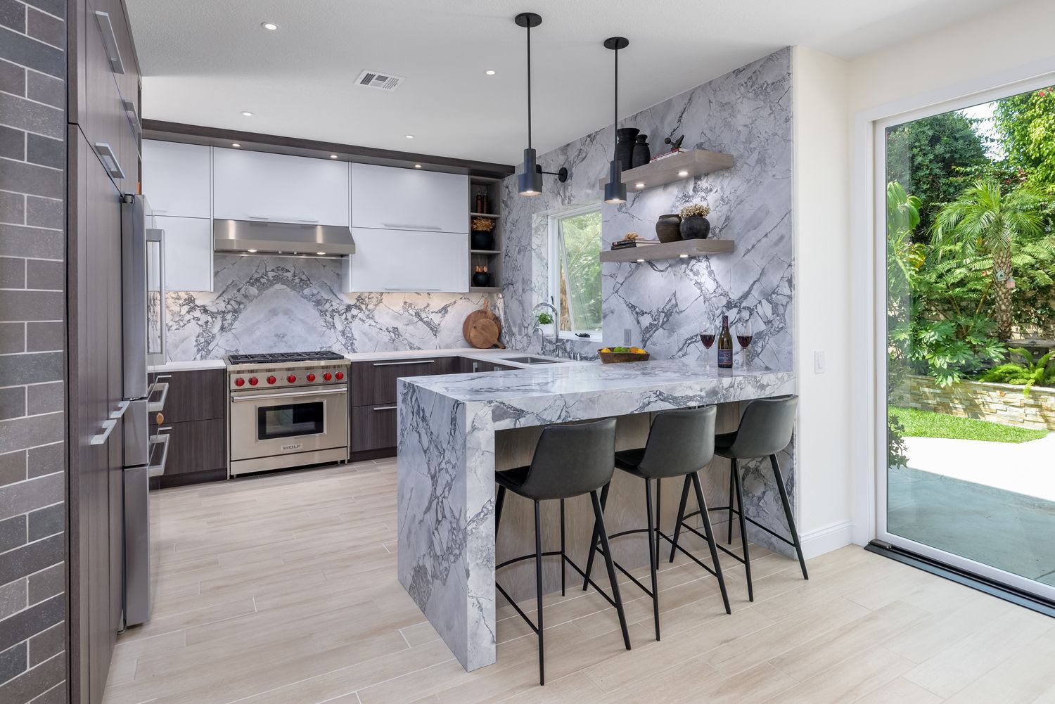 Modern kitchen with marble island, gray barstools, stainless stove, and large window to a green yard