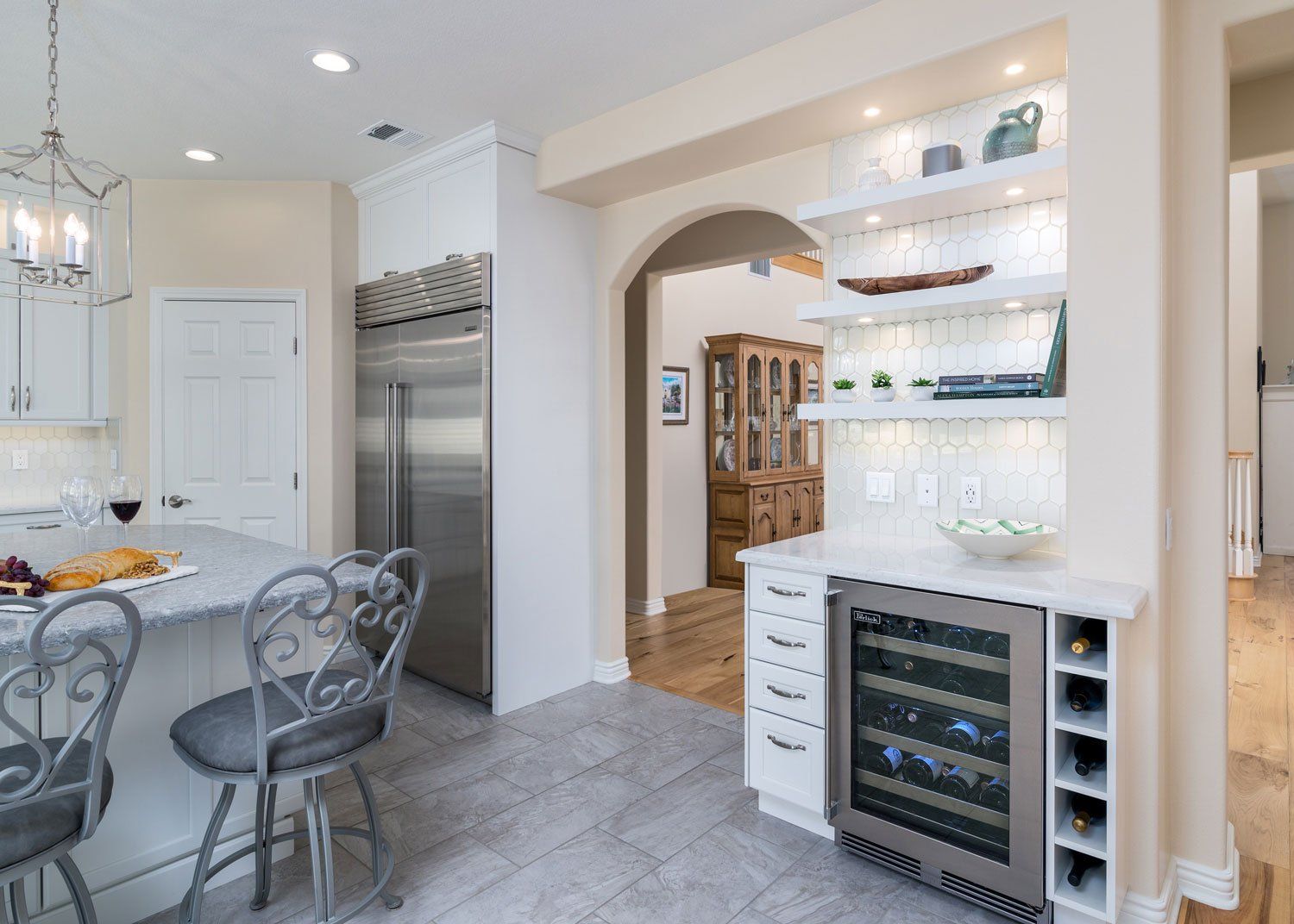 Bright modern kitchen with stainless fridge, arched pass-through, dining table, and wine cooler cupboard