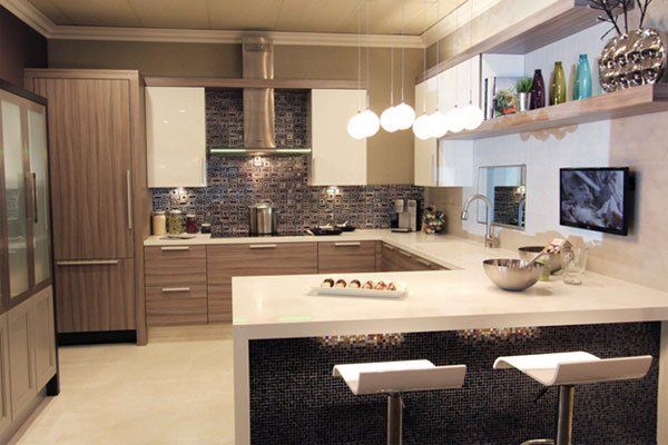 Modern kitchen with light wood cabinets, white island, hanging globe lights, and two stools