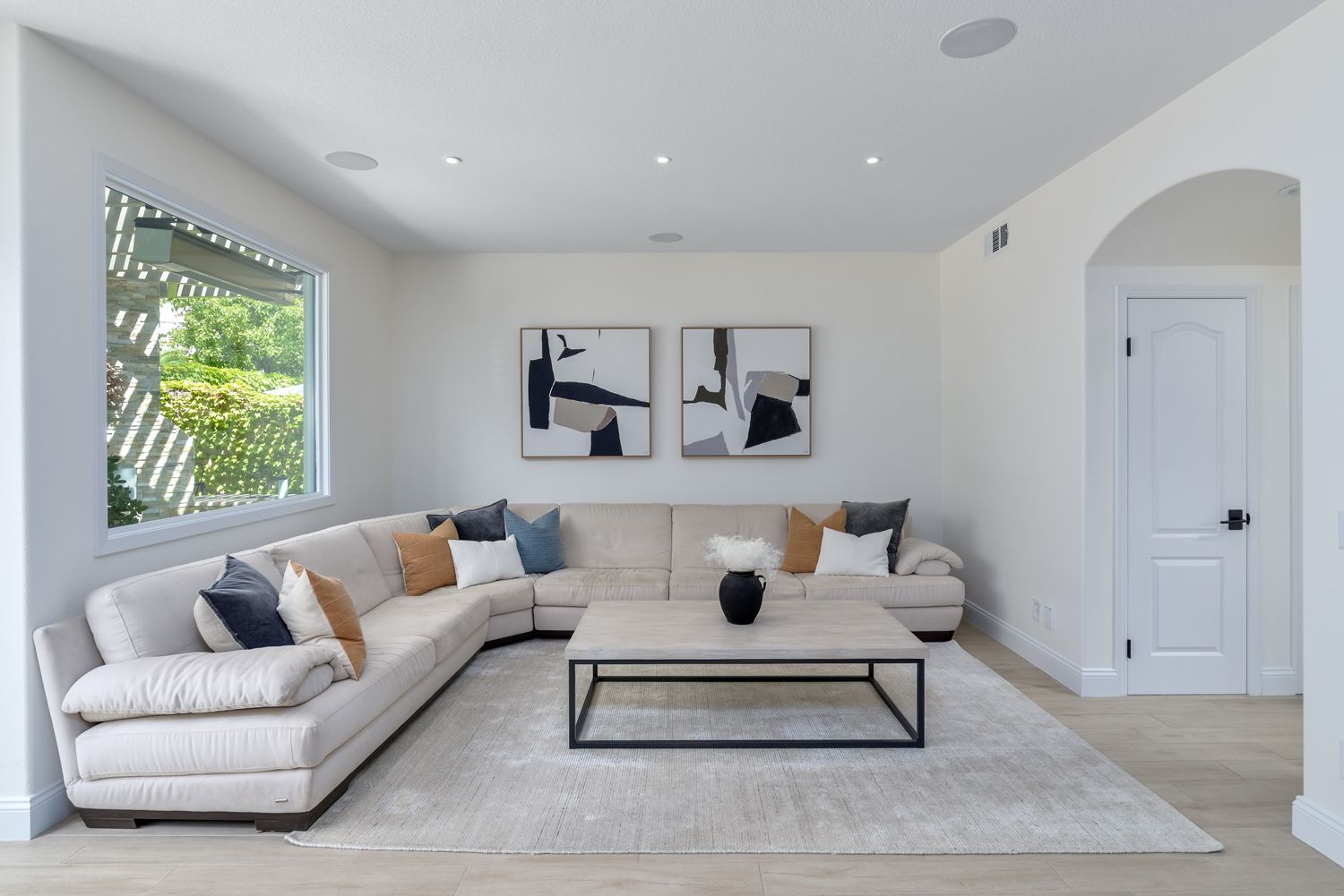 Bright modern living room with beige sectional sofa, abstract wall art, and large window light.