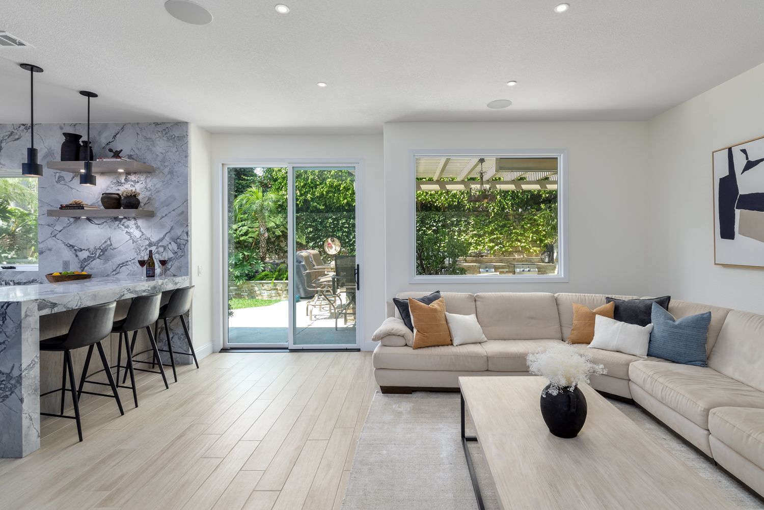 Bright modern living room with beige sectional, kitchen island, and glass doors to a green patio