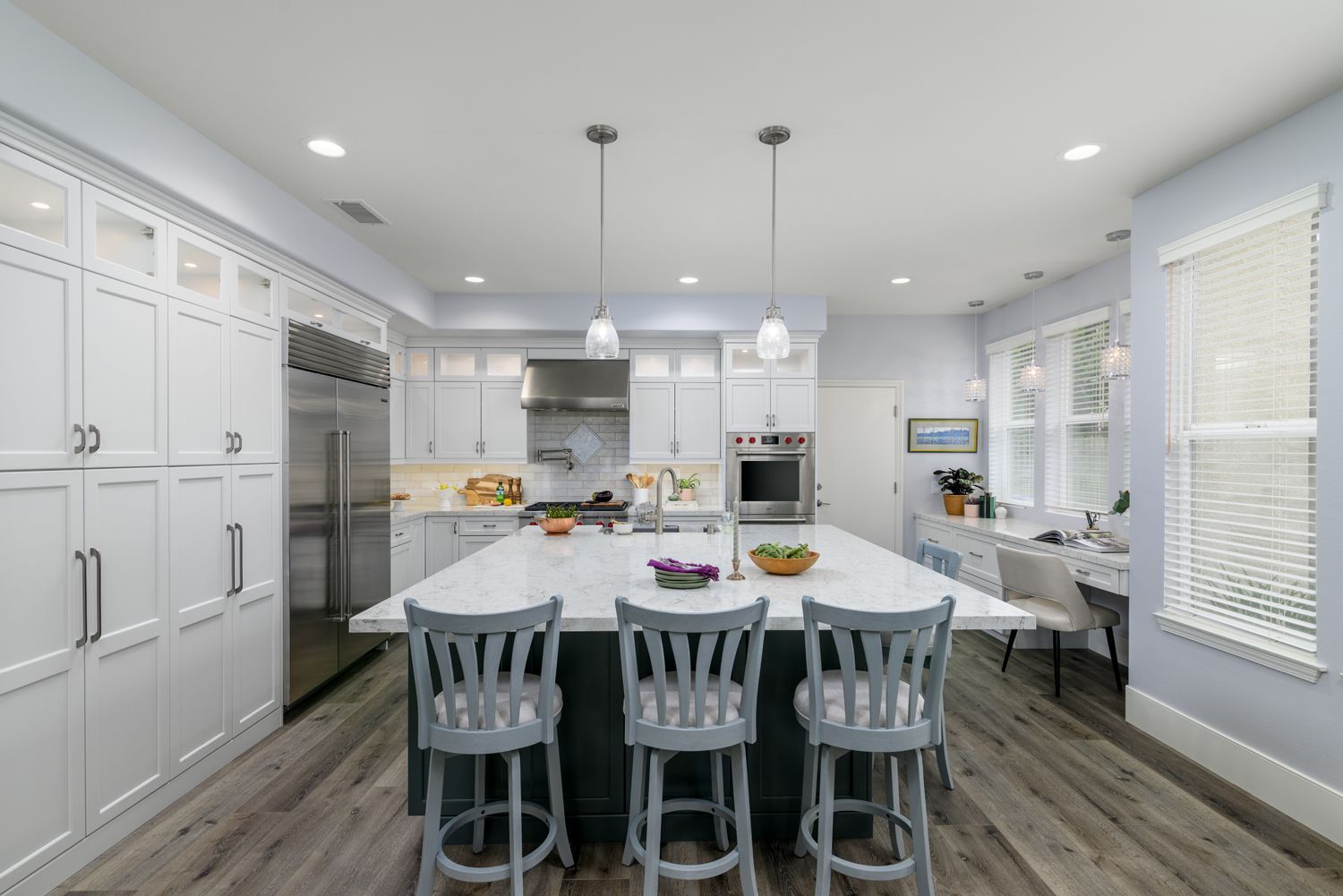 Bright modern kitchen with a large white island, gray stools, stainless appliances, and wood floors.