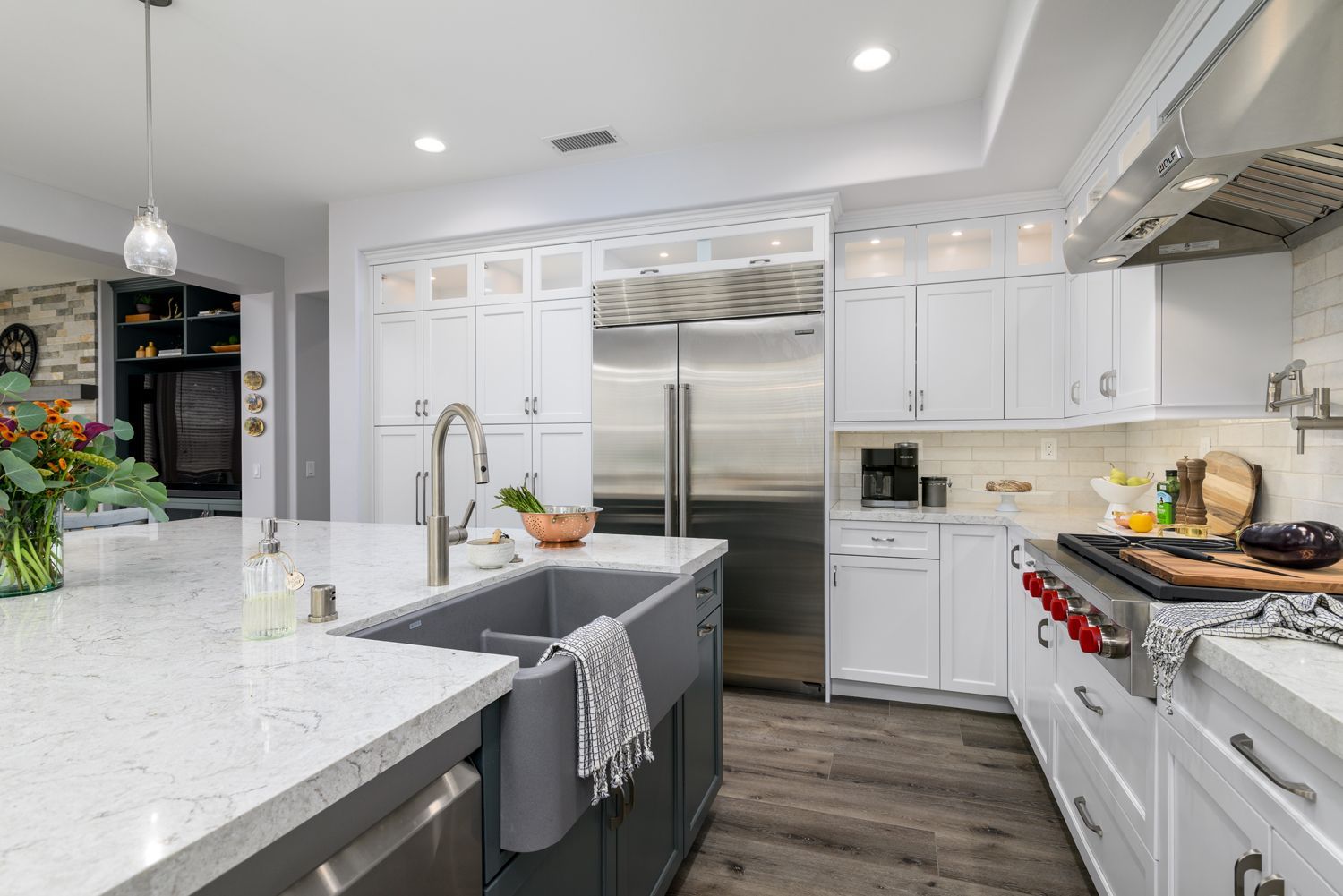 Modern white kitchen with island, stainless steel appliances, and gray barstool to the left