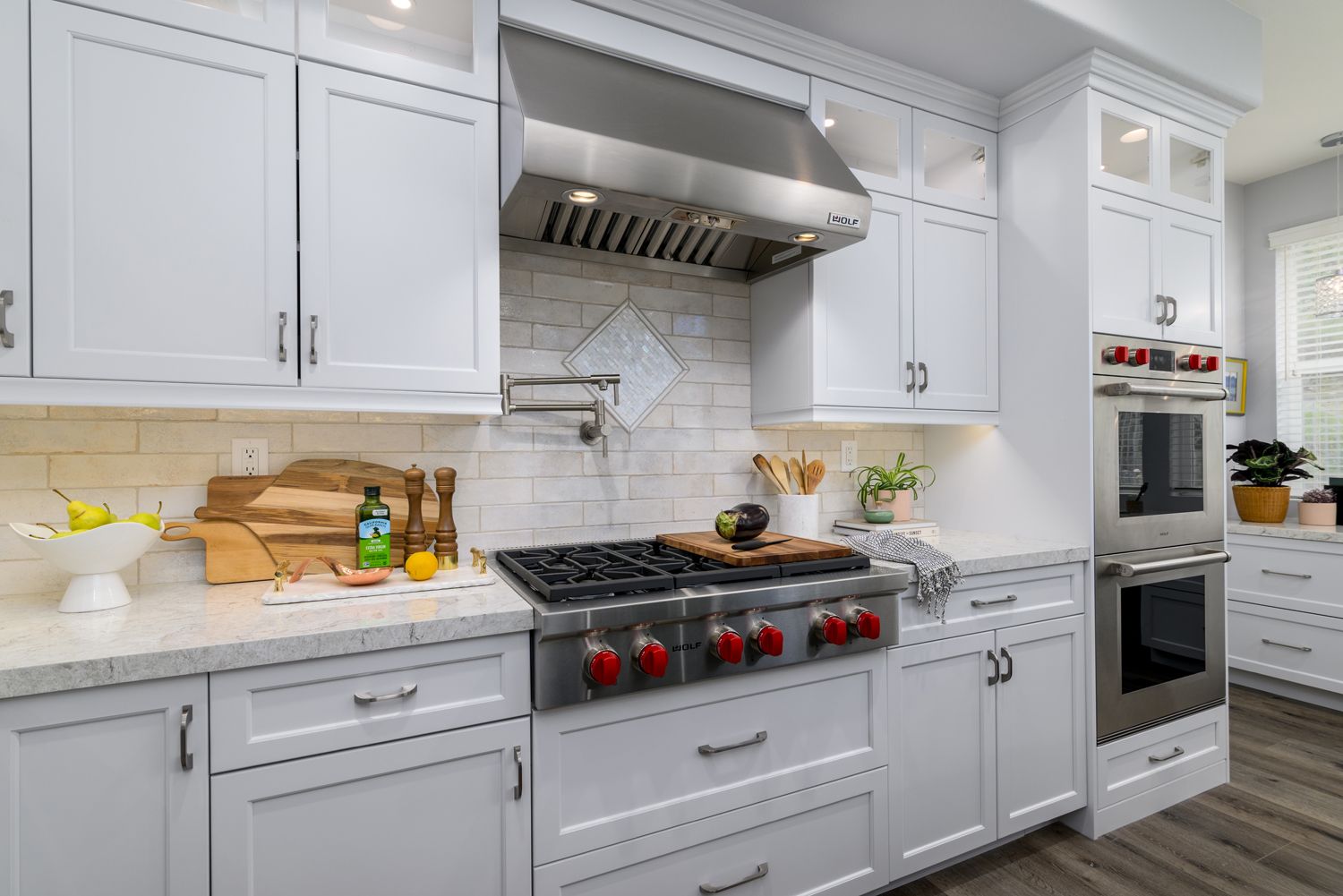 Bright white kitchen with marble counters, stainless range, and red stove knobs