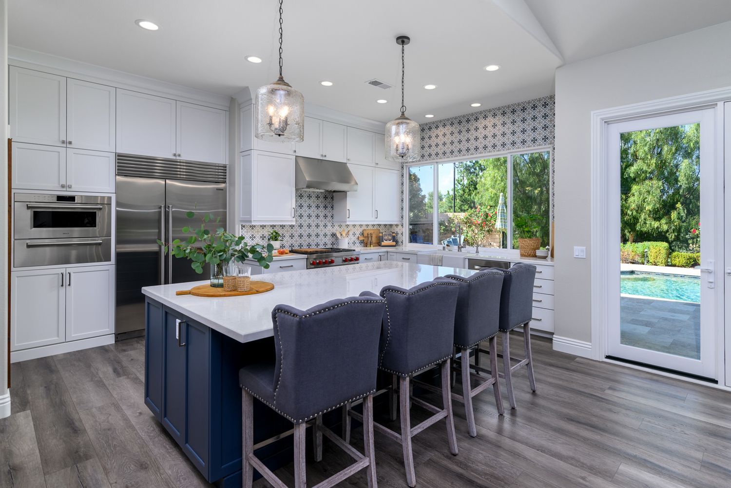 Modern white kitchen with navy island seating, pendant lights, stainless appliances, and sliding glass door to patio