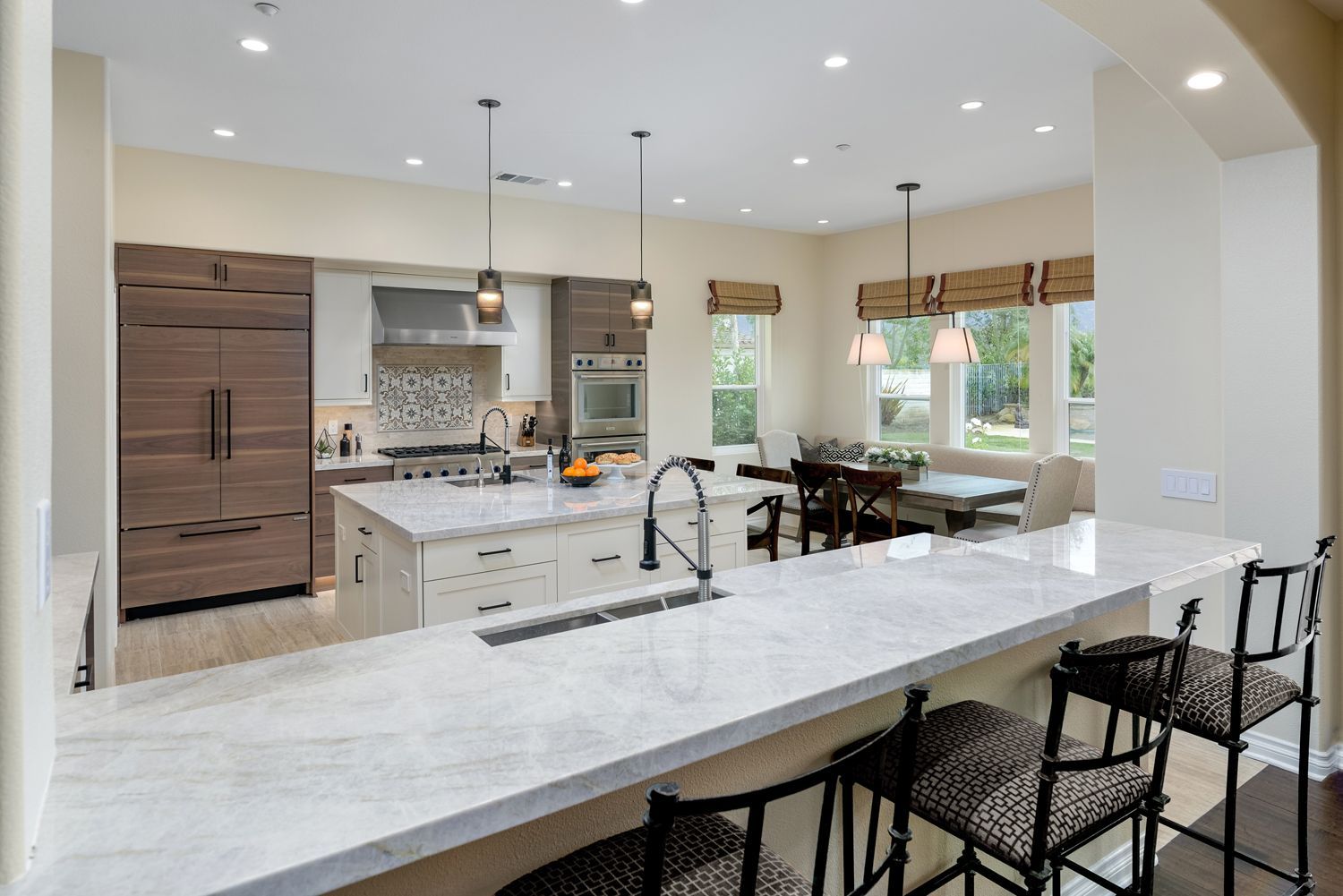 Bright open kitchen with white island, marble countertops, dark bar stools, and dining area by large windows