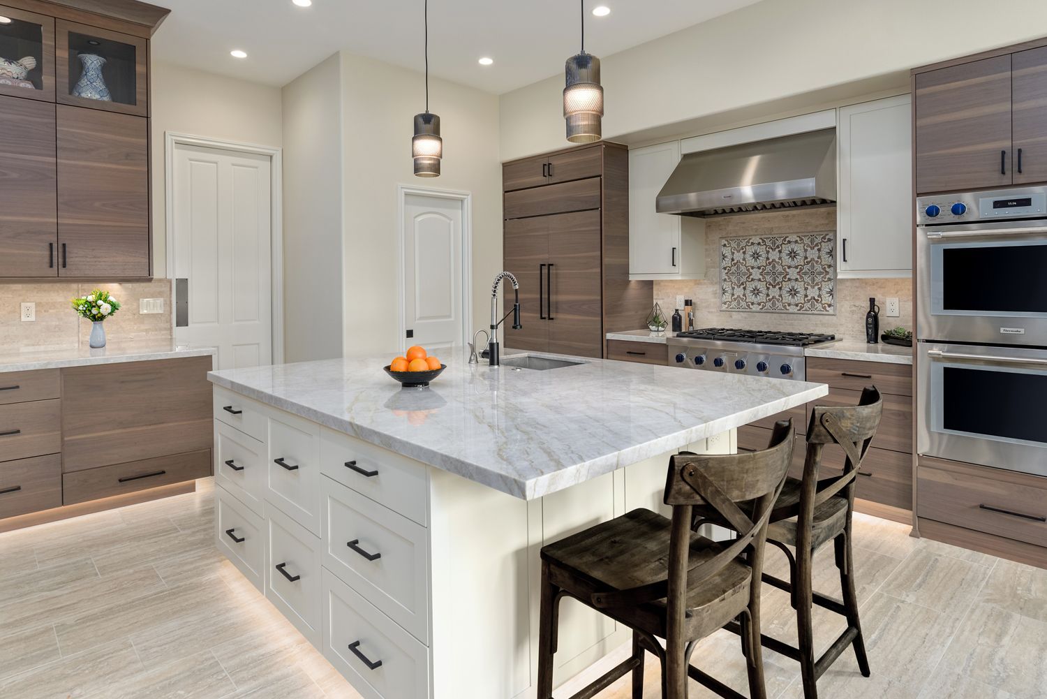 Modern kitchen with large marble island, wood cabinetry, pendant lights, and built-in stainless appliances