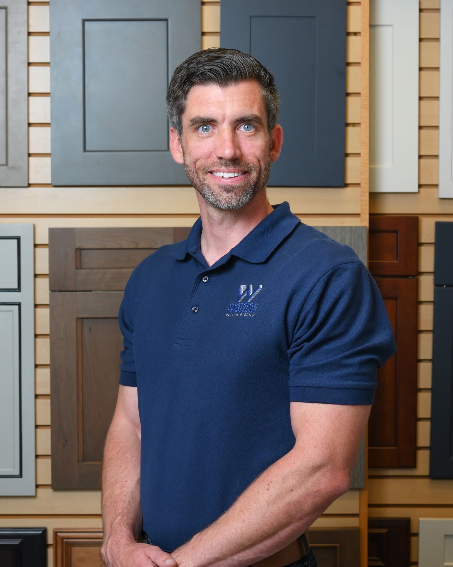 Man standing indoors in a navy polo shirt, smiling in front of sample cabinet doors.