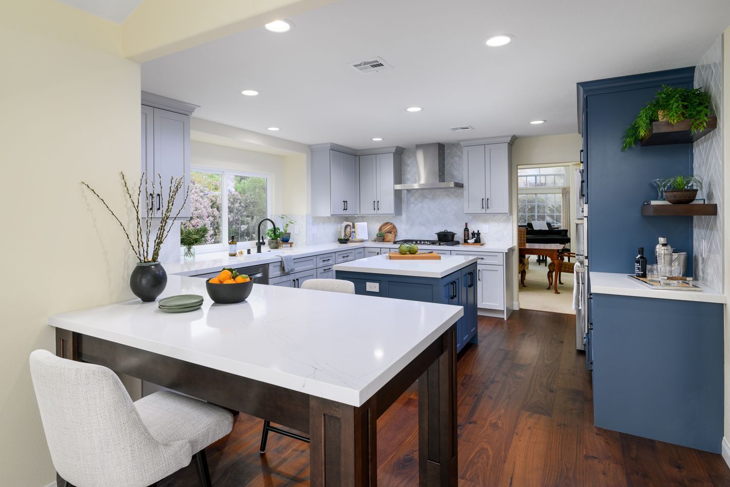 Bright modern kitchen with blue island, white counters, dark wood floor, and dining table by a window