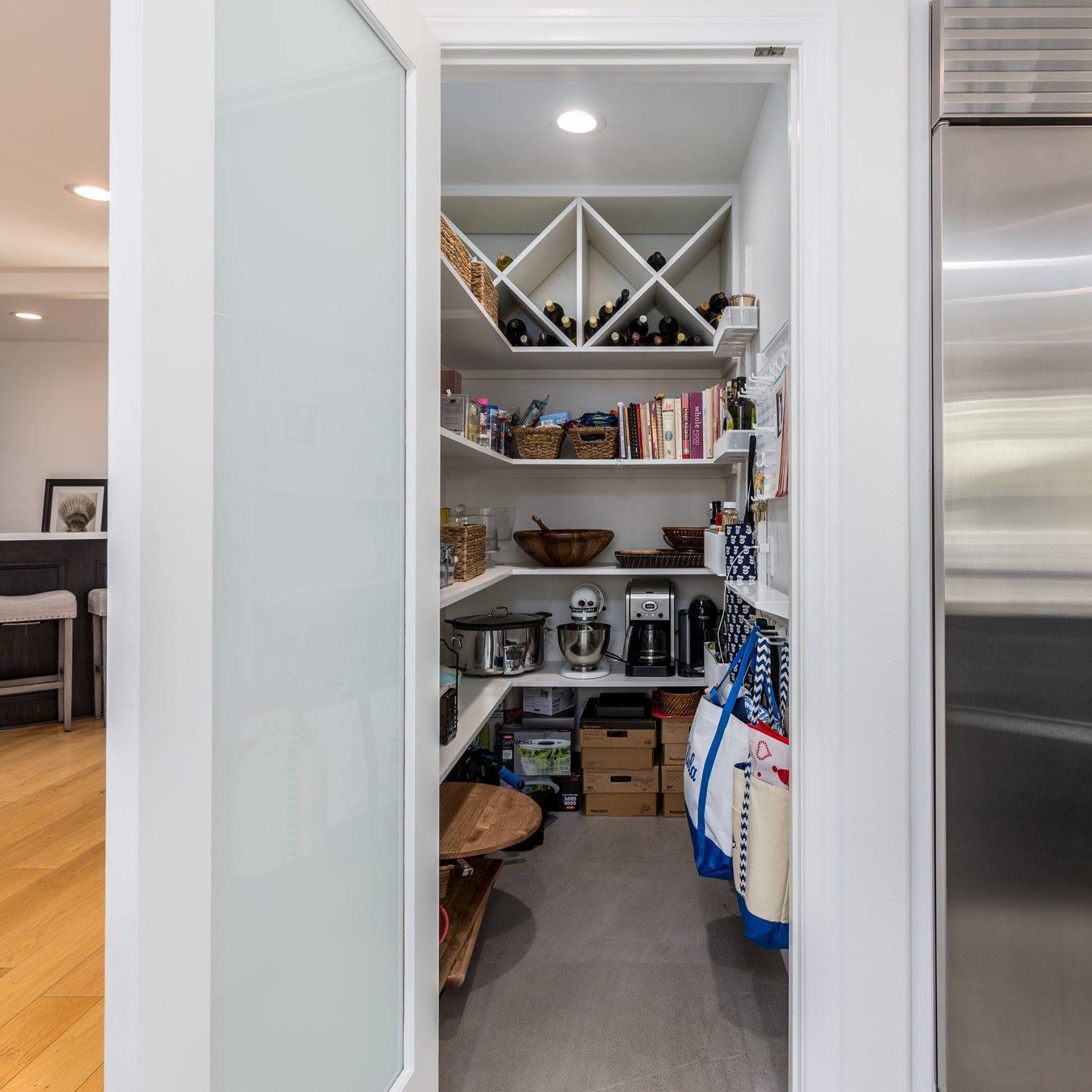 Open pantry with shelves of groceries, bins, and wine rack in a bright kitchen.