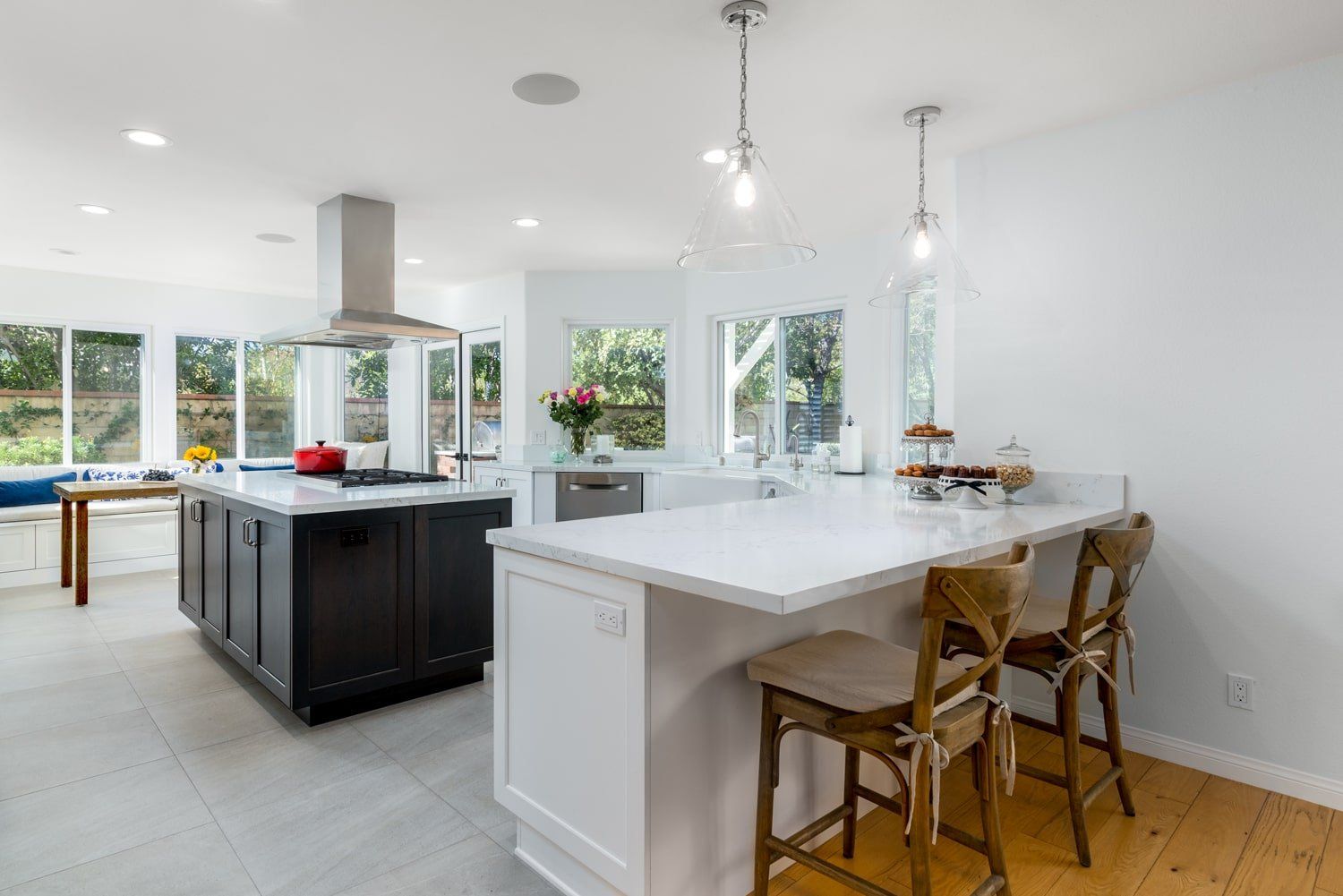 Bright modern kitchen with white island, wooden stools, and large windows overlooking a yard