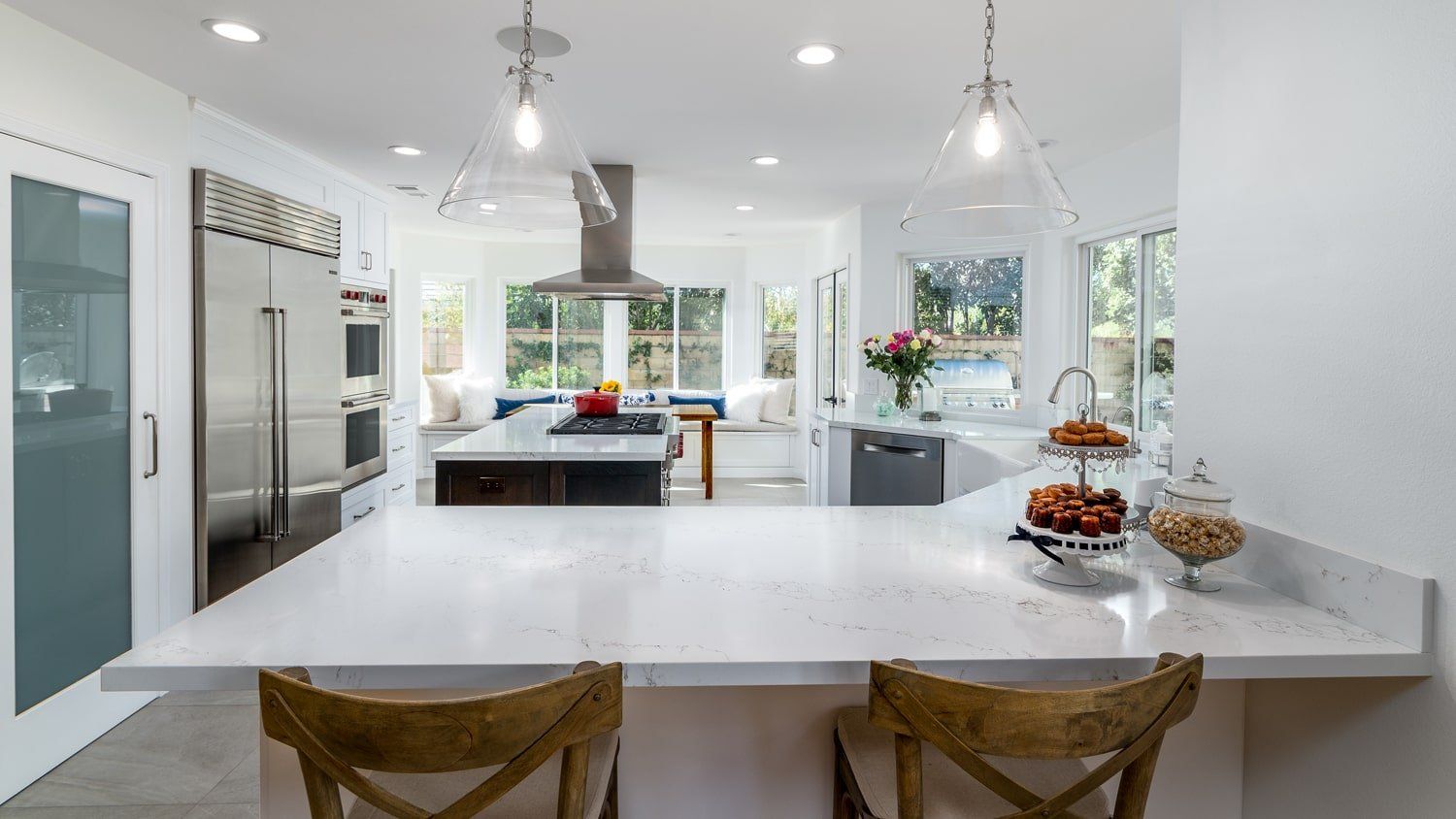 Bright modern kitchen with white countertops, island seating, stainless appliances, and pendant lights