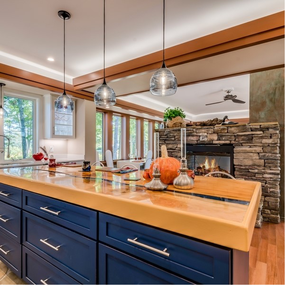 Modern kitchen with blue island, pendant lights, and a stone fireplace by large windows
