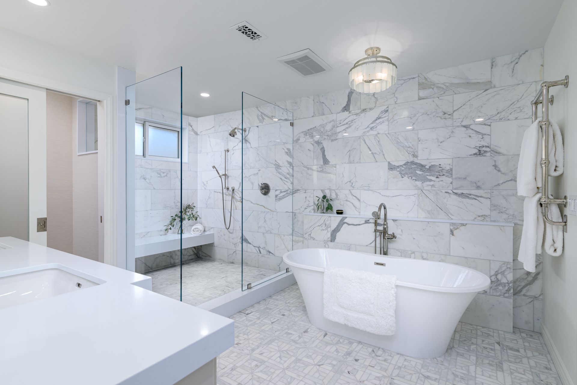 Marble-clad primary bathroom with freestanding tub, glass shower with floating bench and hidden linear drain, and heated towel warmer, Morrison Estates Sutton Valley Oak Park remodel by Westside Remodeling