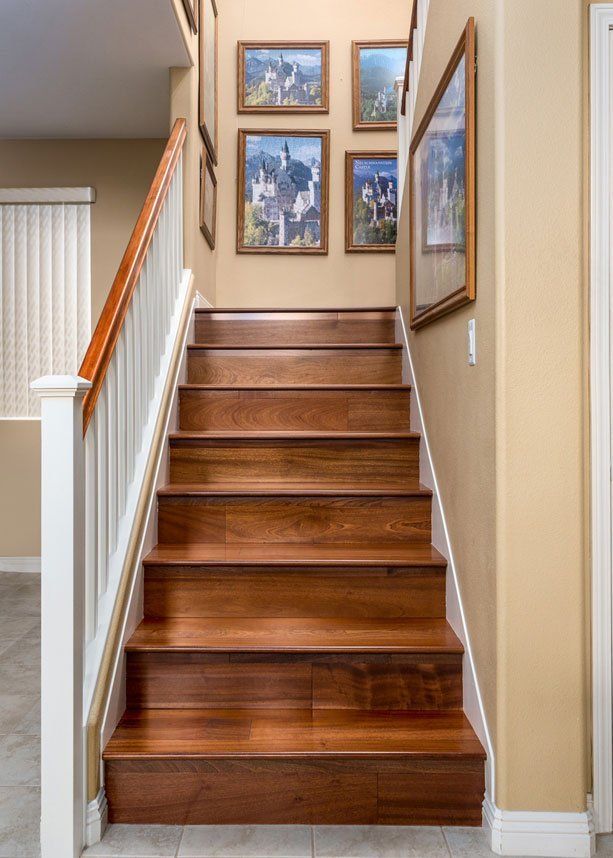 Wooden staircase in a beige hallway with framed wall art and white railing