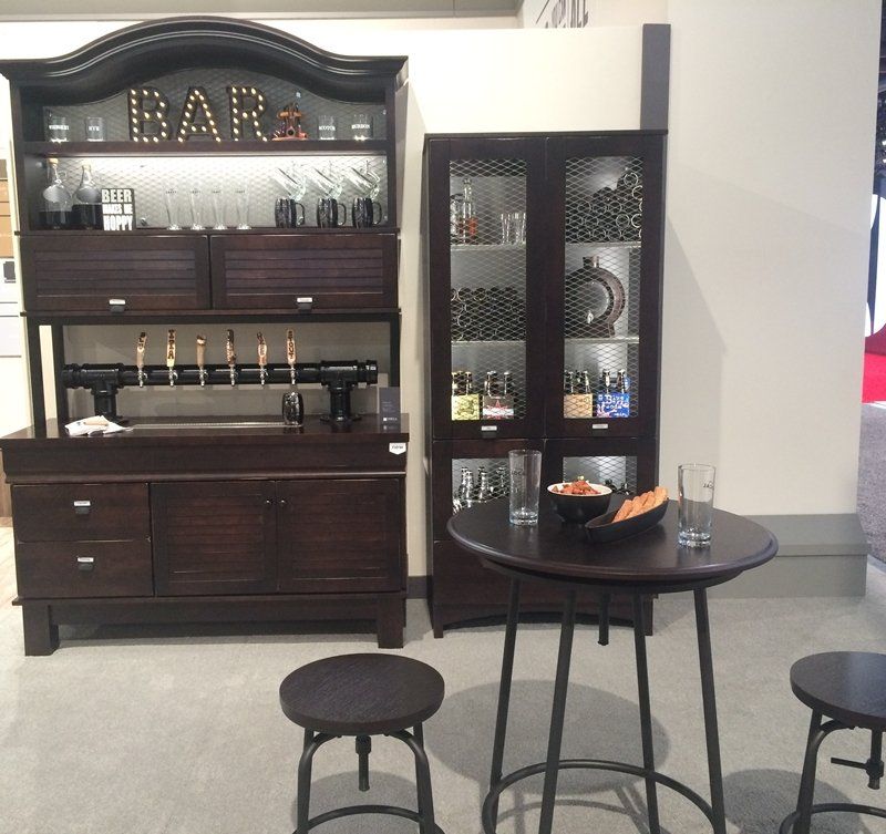 Dark wood home bar cabinet with glasses and taps beside a small round table and stools