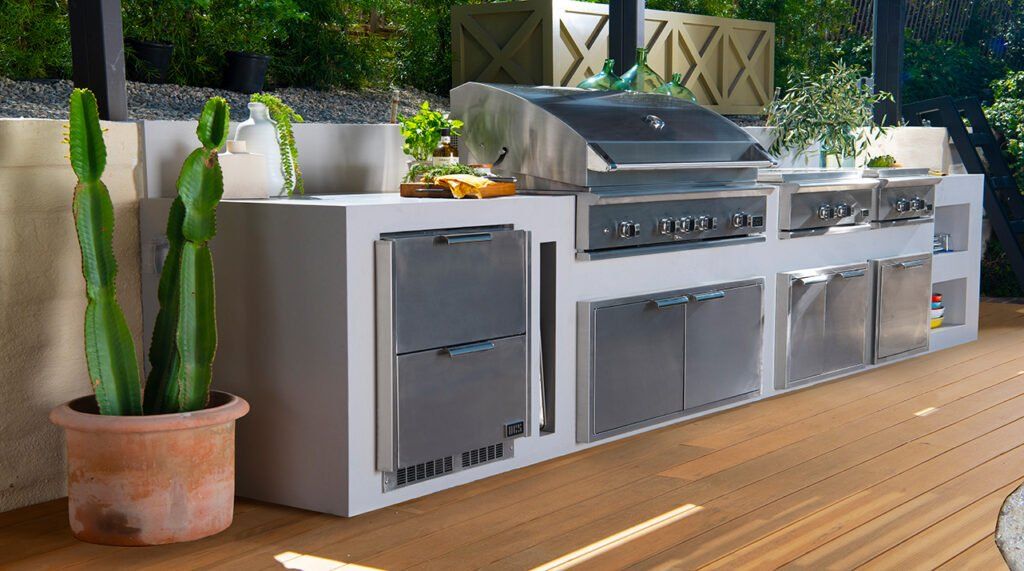 Outdoor patio kitchen with stainless steel grill, white cabinets, and potted cactus plants
