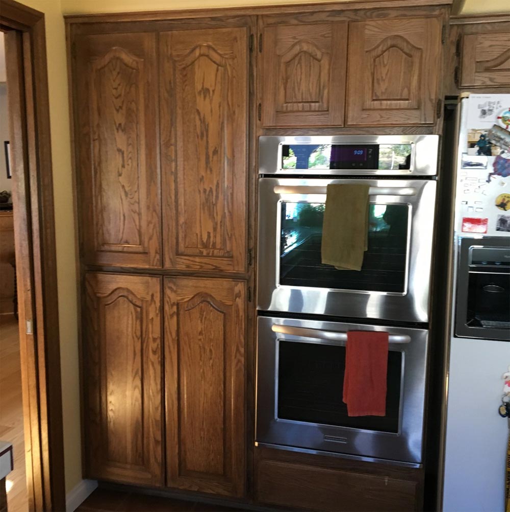 Wooden kitchen cabinets beside a stainless steel double oven with towels hanging on the doors