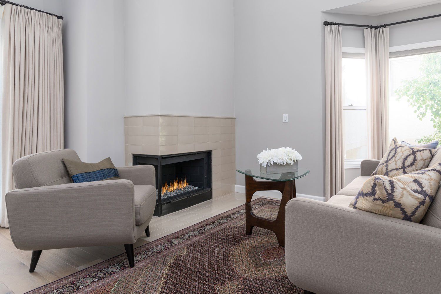 Modern living room with fireplace, beige armchairs, patterned rug, and bright window