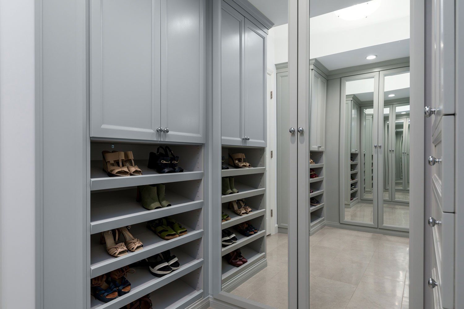 Walk-in closet with mirrored doors and shelves of shoes in a gray interior