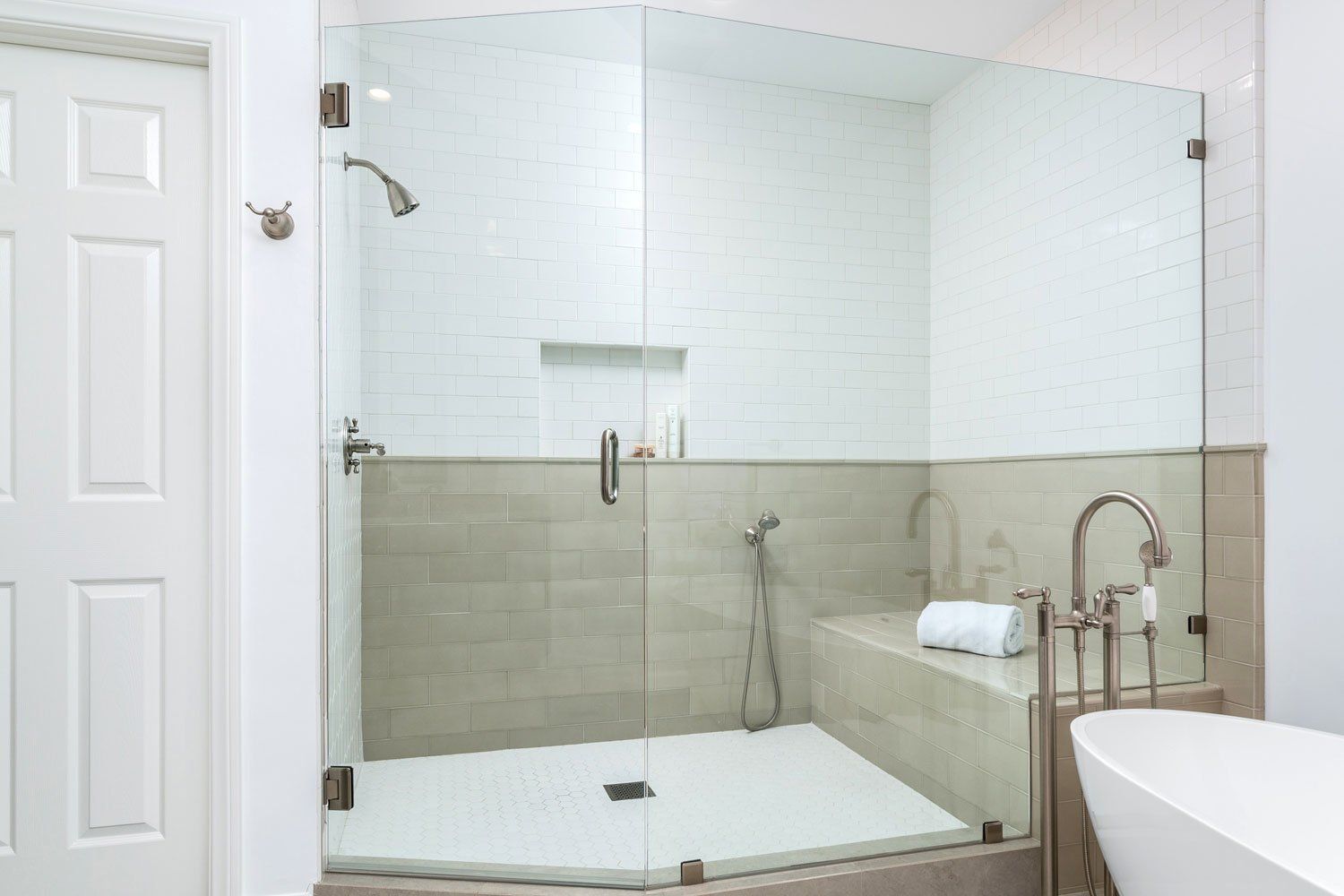 Modern bathroom with glass shower enclosure, white tile, and beige accent wall