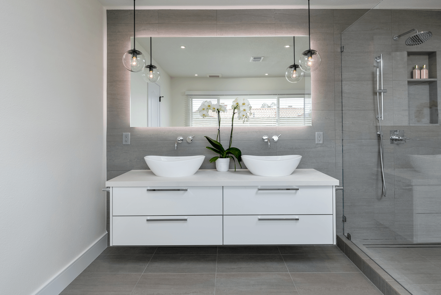 Modern bathroom vanity with double sinks, wall mirror, pendant lights, and glass shower