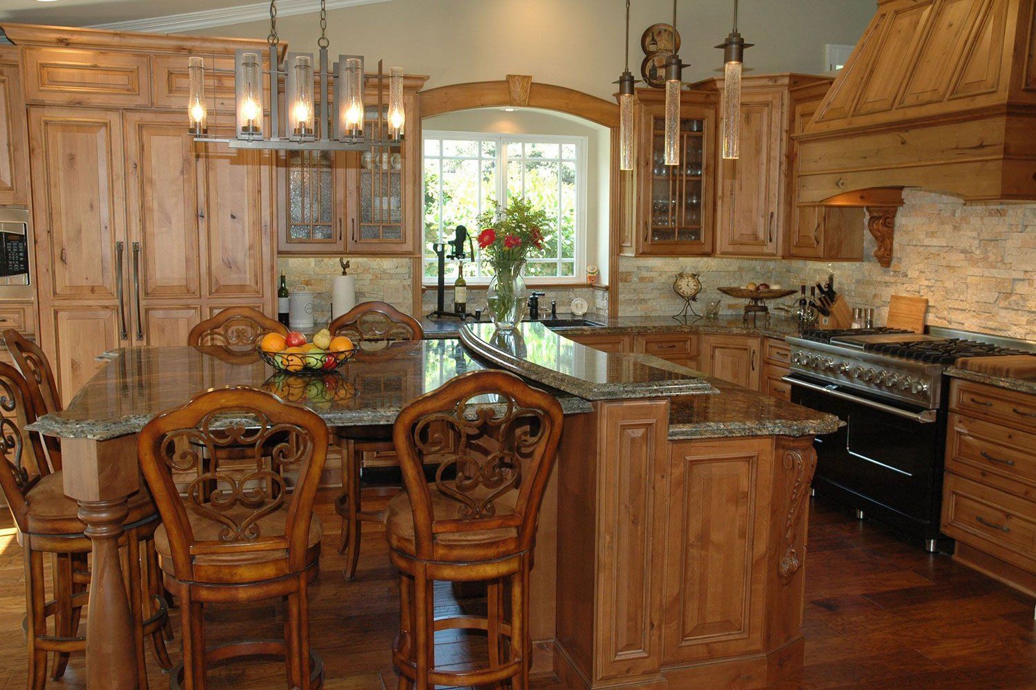 Wooden kitchen with granite island, ornate cabinets, stove, and a vase of flowers by the window