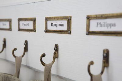 Wall hooks with hanging fabric tags beneath framed name labels on a light-colored wall
