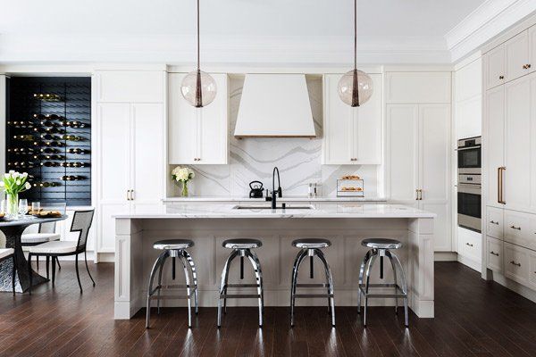 Bright white modern kitchen with marble island, four stools, pendant lights, and dark wood floors