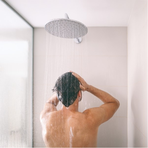 Person showering under a rain shower head in a bright bathroom, seen from behind