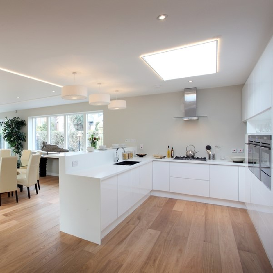 Bright modern white kitchen with wood floors, island, skylight, and dining area by large windows