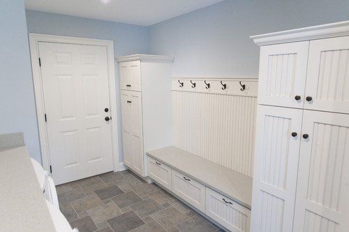 White mudroom with built-in bench, hooks, cabinets, and tile floor.