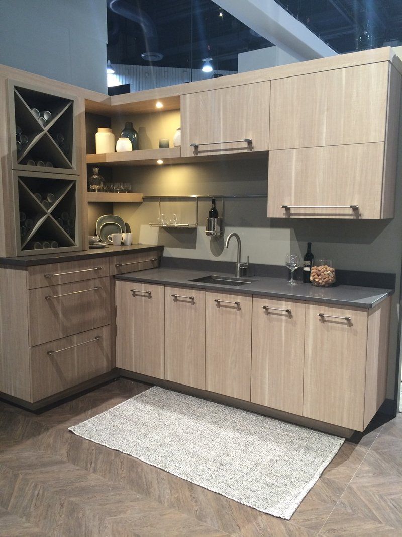 Modern wood kitchen display with cabinets, countertop, sink, and herringbone floor in a showroom
