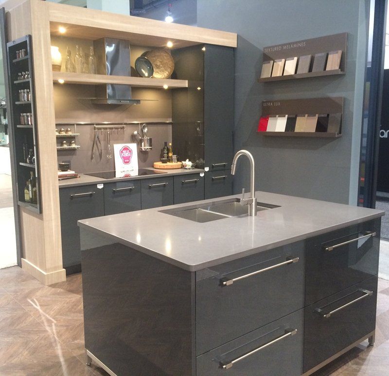 Modern kitchen showroom with dark cabinetry, gray island, stainless sink, and open shelving on the wall