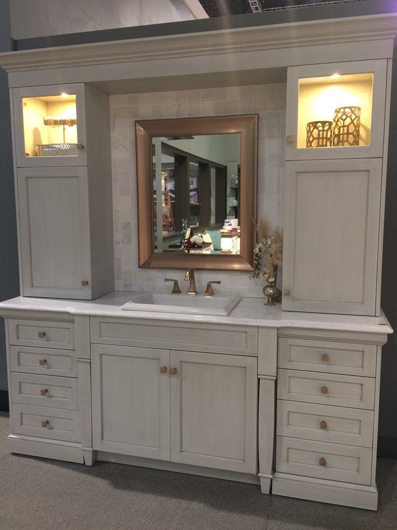 White bathroom vanity with mirror, sink, drawers, and lit display cabinets on both sides.