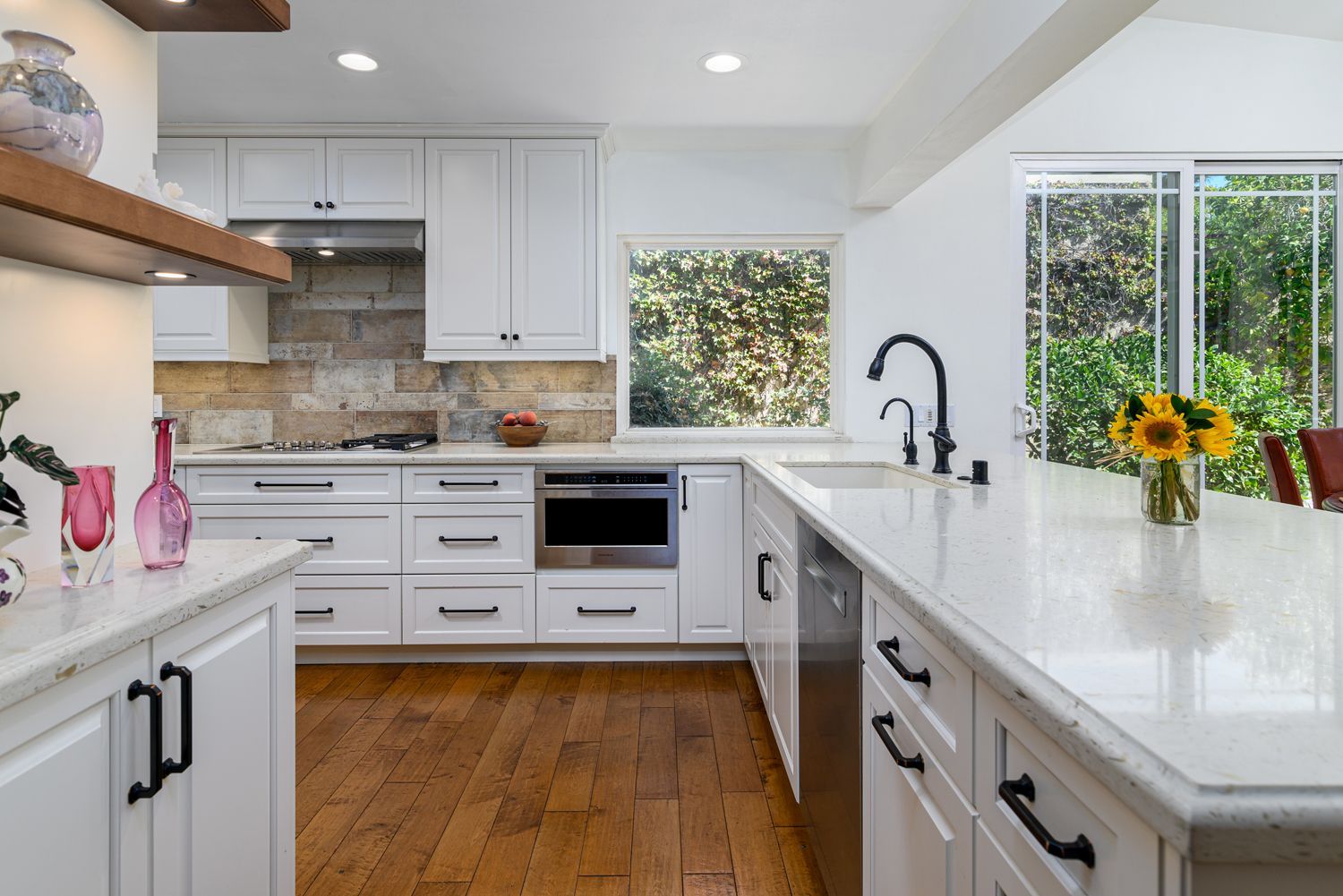 Bright modern kitchen with white cabinets, quartz countertops, wood floor, and a vase of sunflowers.