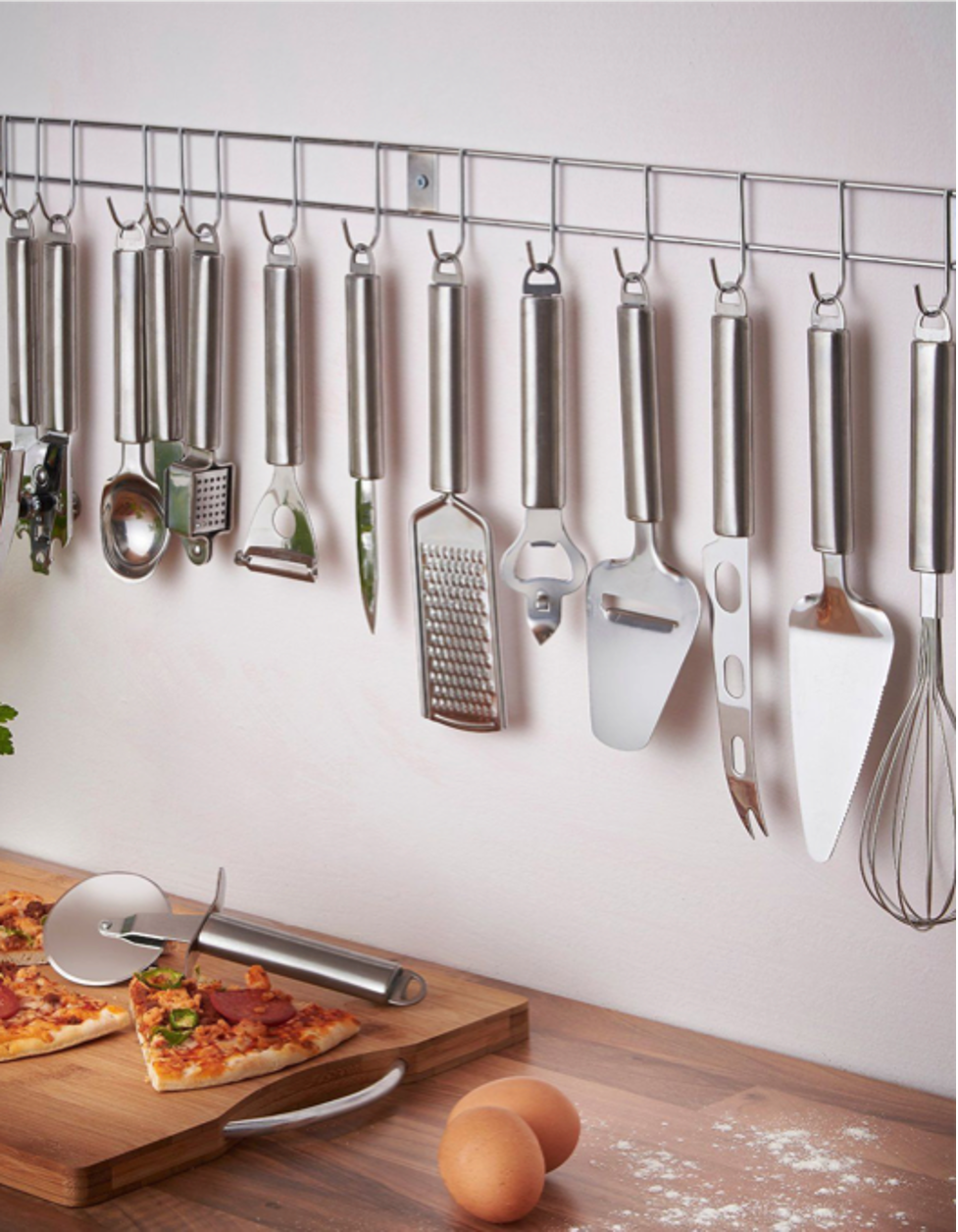 Kitchen utensils hanging on a wall rack above a wooden counter with eggs and a pizza board.